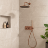 Moderne inbouw doucheset met ronde regendouche en handdouche in geborsteld brons, gemonteerd tegen een lichte marmeren wand in een stijlvolle badkamer.