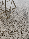 Close-up van Class Terrazzo Mira rec 60x60cm terrazzo tegels keramische met elegant gespikkeld patroon en decoratief metalen object, ideaal als vloertegels binnen.