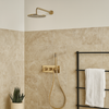 Ingebouwde thermostatische doucheset in geborsteld goud met regendouche, handdouche en wandmontage in een moderne badkamer met beige natuursteen tegels.