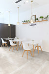 Mystone Chalk Zand keramische tegels in 120x120 cm gelegd in een modern café-interieur met witte stoelen en tafels, ideaal als zandkleurige vloertegels badkamer.