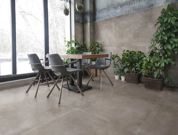 Stijlvolle zithoek met industriële look en Mystone Mud grijs taupe vloertegels 120x120cm. Natuurlijke lichtinval en veel groene planten geven een warme sfeer.