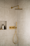 Moderne inbouw doucheset in geborsteld goud met regendouche en handdouche, gemonteerd tegen een lichtgrijze marmeren badkamerwand.