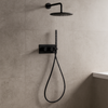 Moderne inbouw doucheset in matzwart met ronde regendouche en handdouche, gemonteerd op een lichtgrijze tegelwand in een minimalistische badkamer, met zacht stromend water zichtbaar.