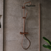 Stortdoucheset met thermostaatkraan in geborsteld brons gemonteerd in een moderne badkamer met grijze tegels en glazen douchewand.