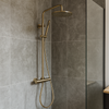 Stortdoucheset met thermostaatkraan in geborsteld goud gemonteerd in een moderne badkamer met grote grijze wandtegels en een glazen douchewand.