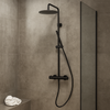 Stortdoucheset met thermostaatkraan in gunmetal afwerking geïnstalleerd in een moderne badkamer met grijze wandtegels, glazen douchewand en minimalistisch interieur.