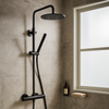 Mat zwarte stortdoucheset met thermostaatkraan gemonteerd op een moderne grijs betegelde badkamerwand, met een glazen planchet en een mat raam voor natuurlijk licht.